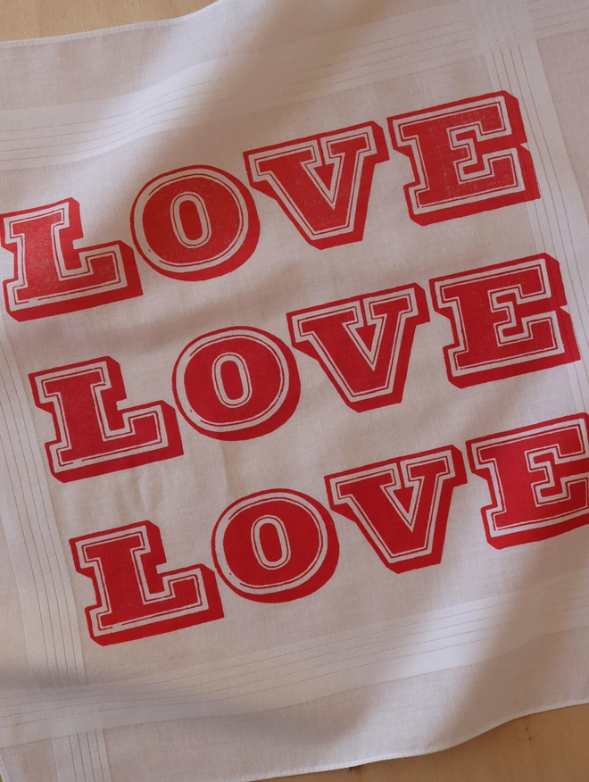 A close up detail photo of a Mr.PS Love Love Love handkerchief screenprinted is 3 shades of red: coral pink, raspberry and bright red.