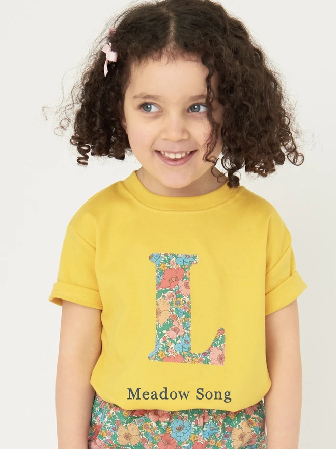 a yellow t-shirt with a floral initial on front