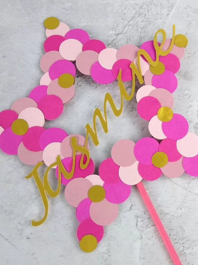 Pink personalised name topper. Mixed pink and gold dots decorate a star outline. Jasmine is written in gold italic script across the centre of the star.