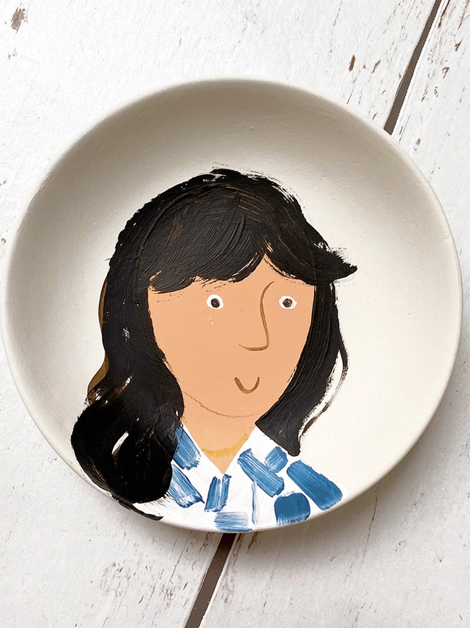 small white plate with stylised painted portrait of girl with blue and white shirt