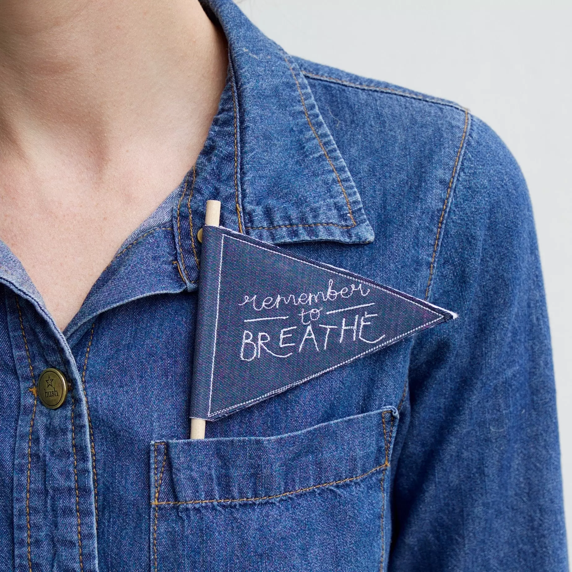 Woman wearing denim shirt with remember to breathe pennant in top pocket
