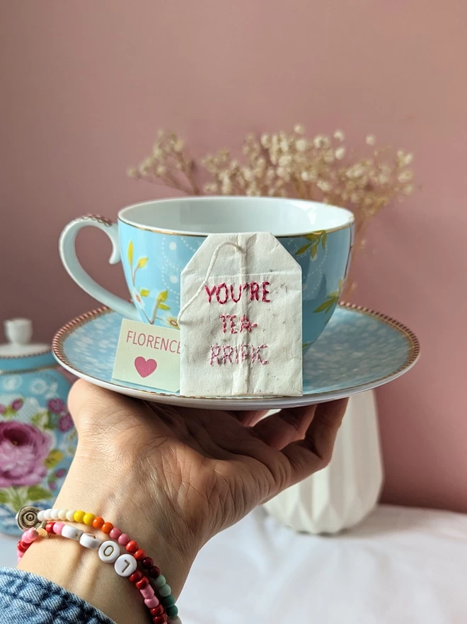 Embroidered You're tea-rrific teabag held on cup and saucer 