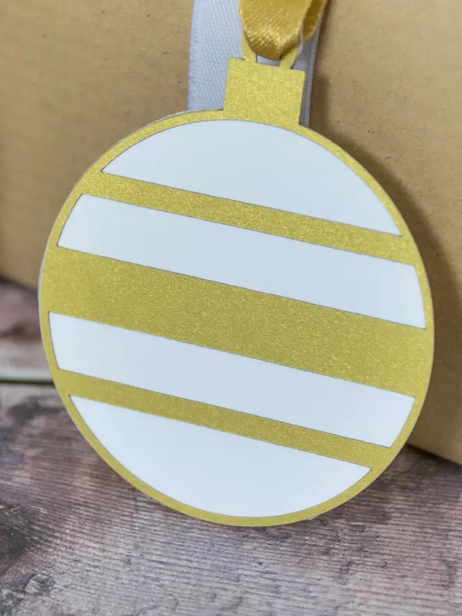 Closeup of paper bauble gift tag with gold and white horizontal stripesGold and White Christmas Bauble Gift Tag