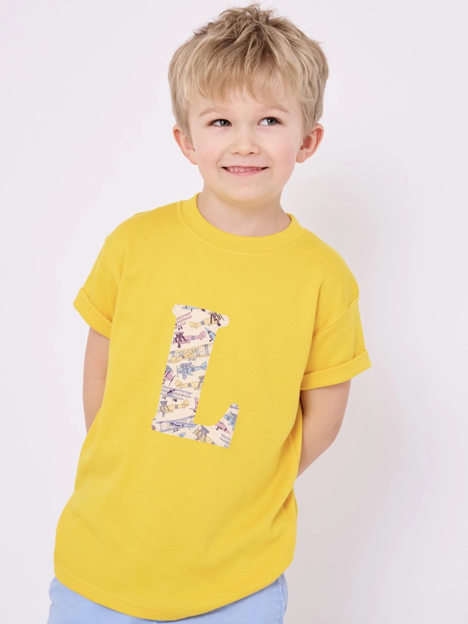 a little boy in yellow t-shirt with vintage jets print initial on front