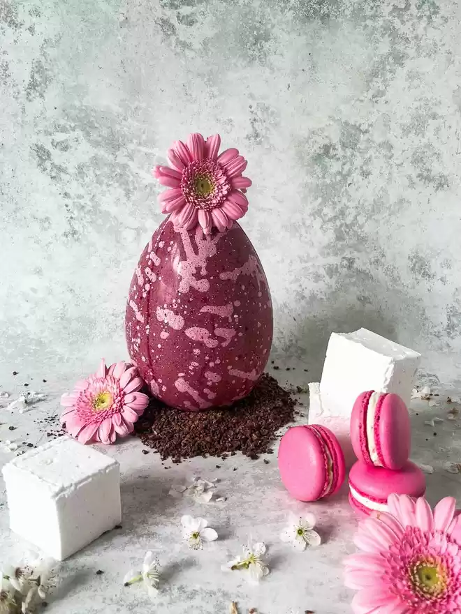 a pink easter egg with flowers and  pink toasted marshmallow filled macarons on a table with giant marshmallows and  pink flowers