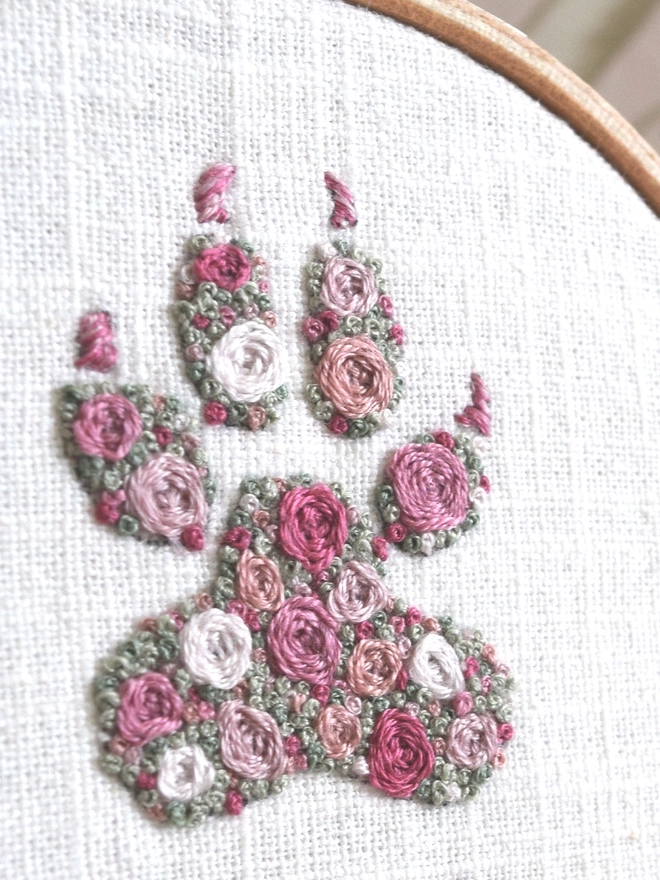 An embroidered Dogs Paw, of woven wheel roses in 5 shades of pink with French Knot green grass. 