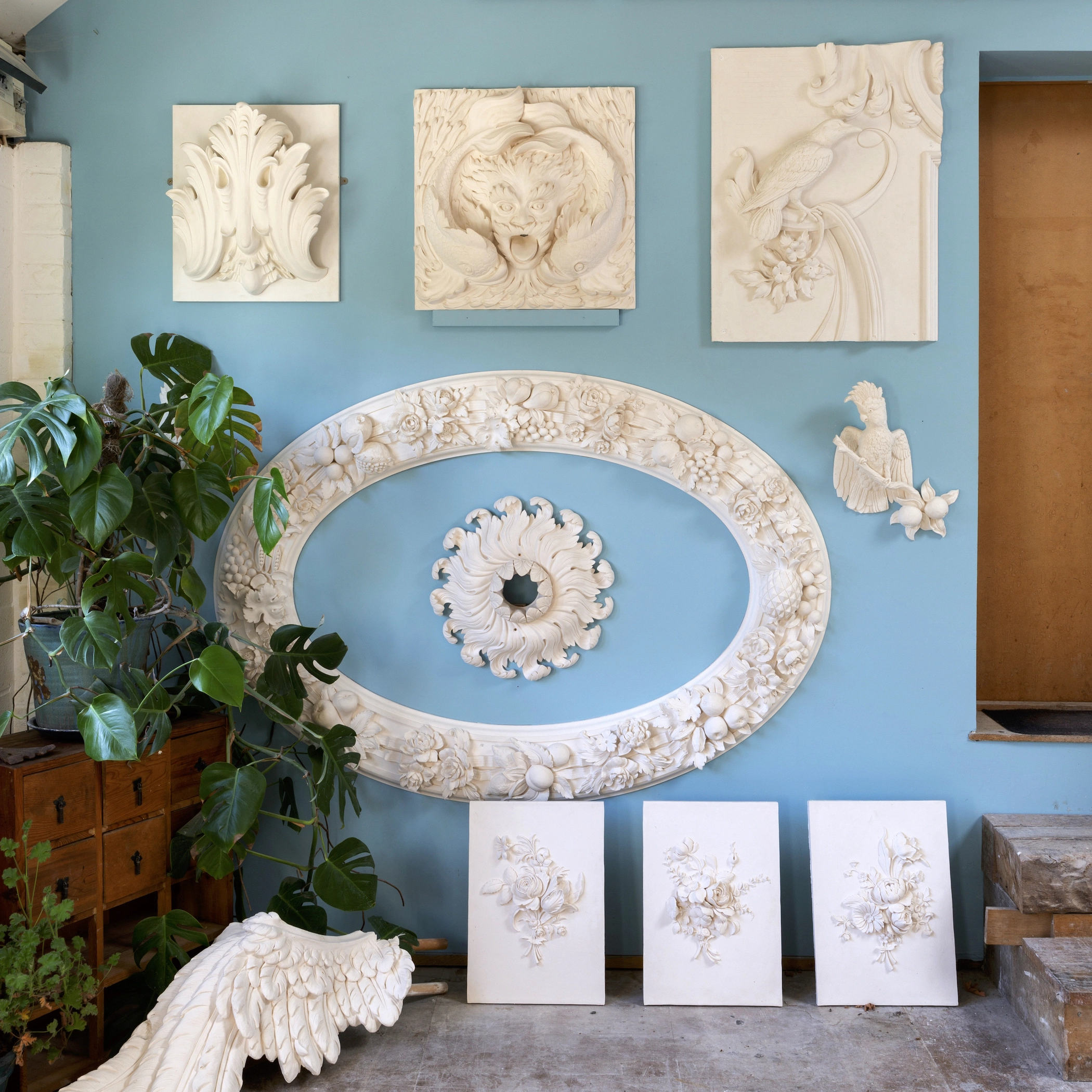 Decorative plaster sculpture displayed on a blue wall with houseplant