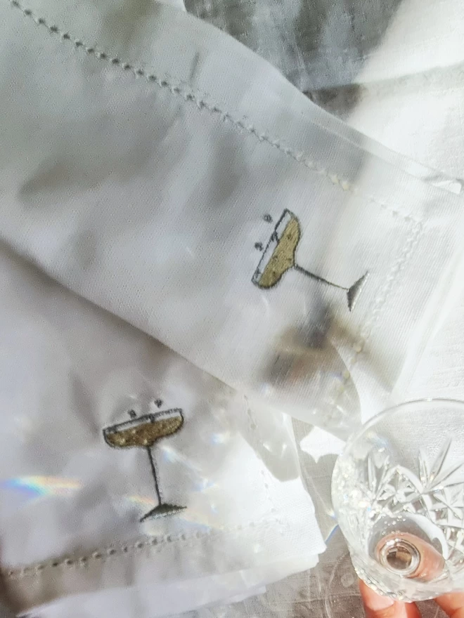 two white napkins with champagne glass motifs embroidered on them on a table