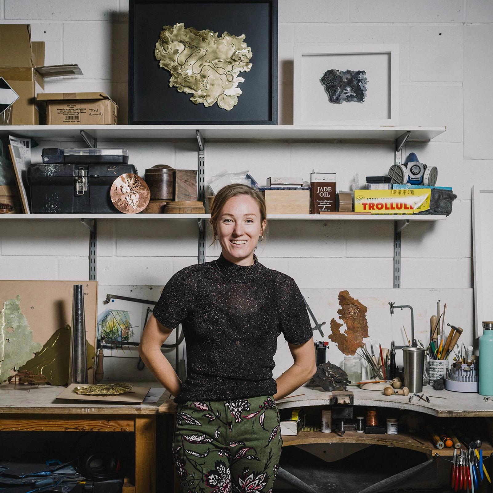 Holly smiling in her Contour Map Collection workshop surrounded by tools and framed map pieces.