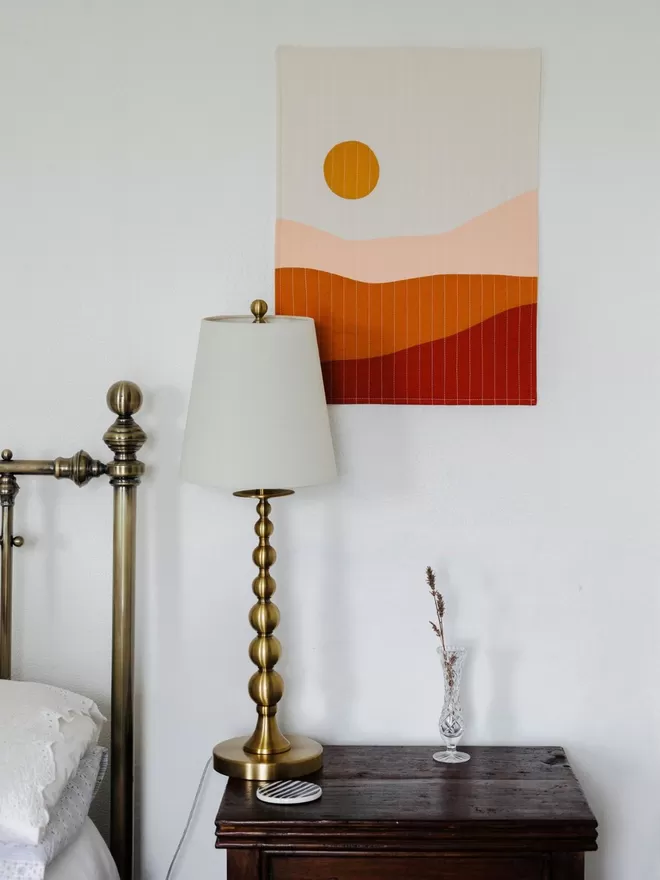 Earth Quilt Hanging On White Wall Beside Bed In Bedroom