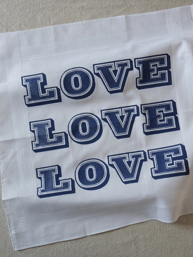 A Mr.PS Love hankie printed in midnight blue laid flat on a linen tablecloth