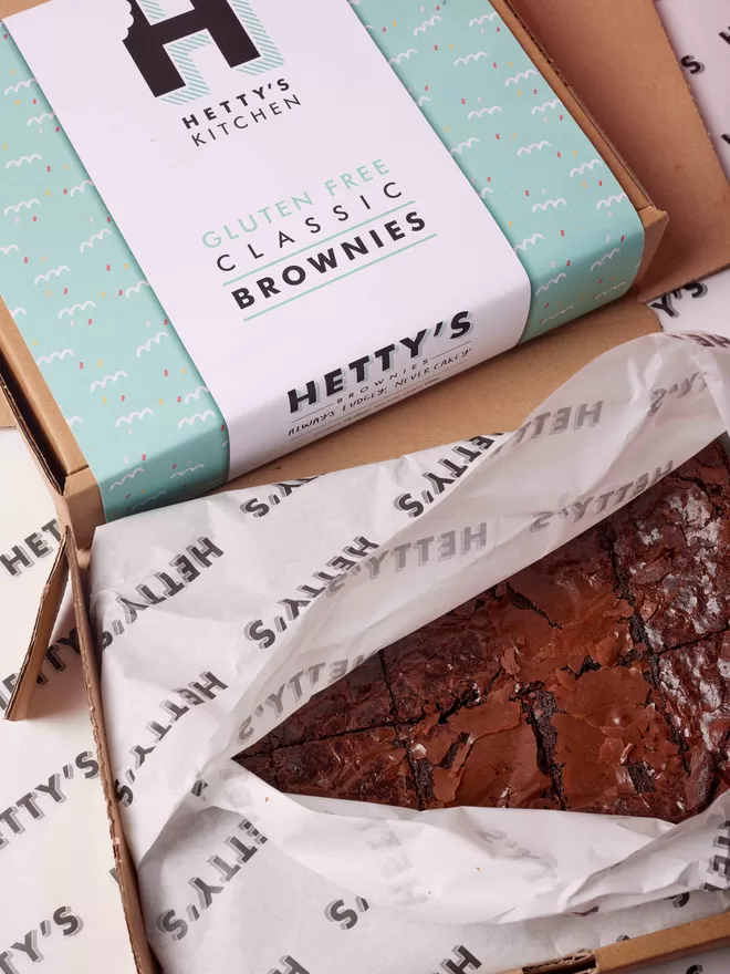 Ten slices of gluten free classic fudge brownies in the branded box packaging they arrive inside