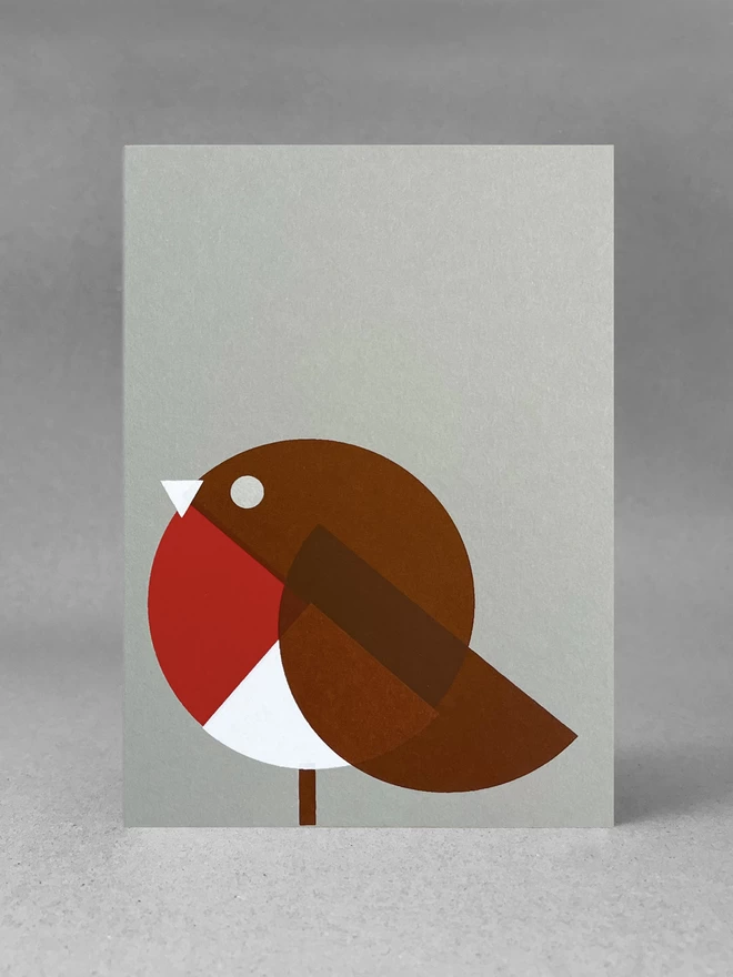 Geometric shapes in red white and brown make up this handprinted robin christmas card, stood front on, in a light grey set.