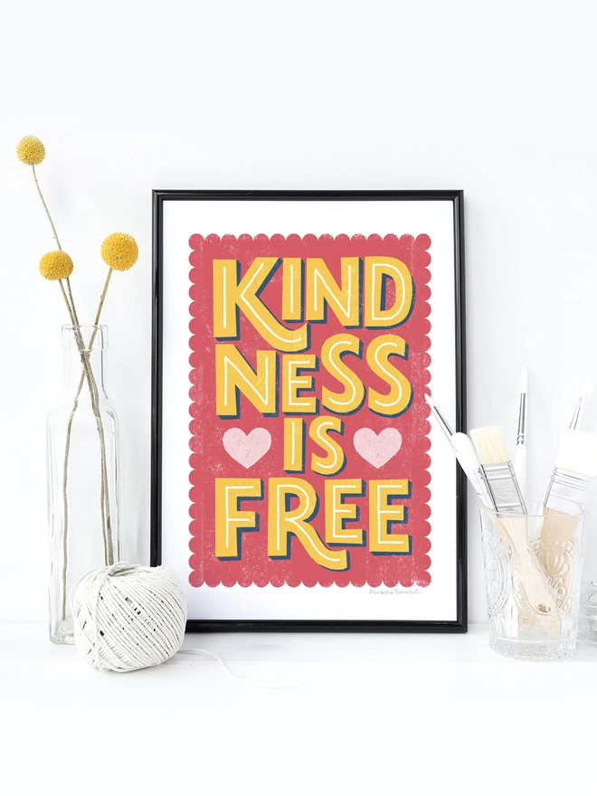 kindness is free typographic print in a black frame with yellow flowers in a clear vase