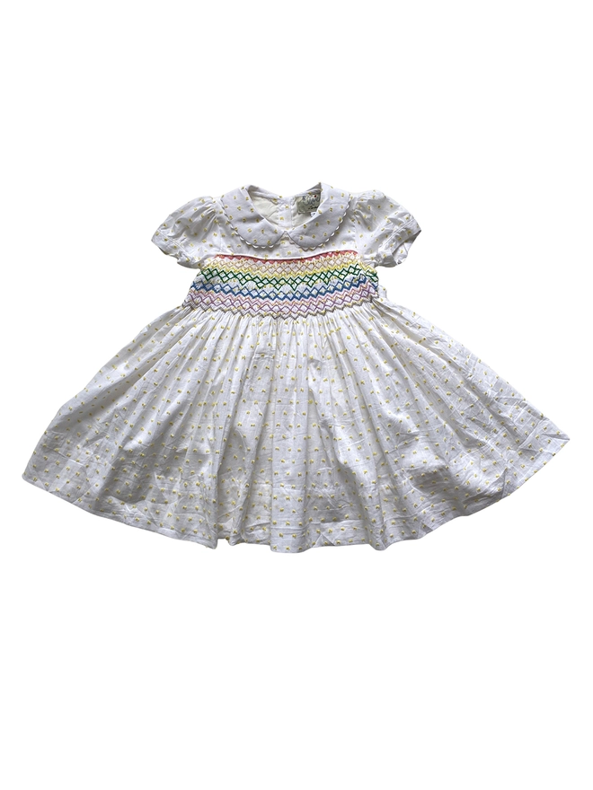A white dress with yellow swiss dots, a peter pan collar and rainbow smocking.