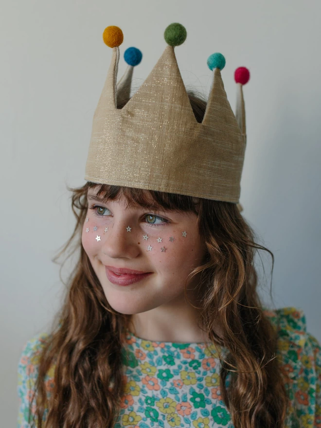 Girl in Gold dressing up crown with wool pom poms 