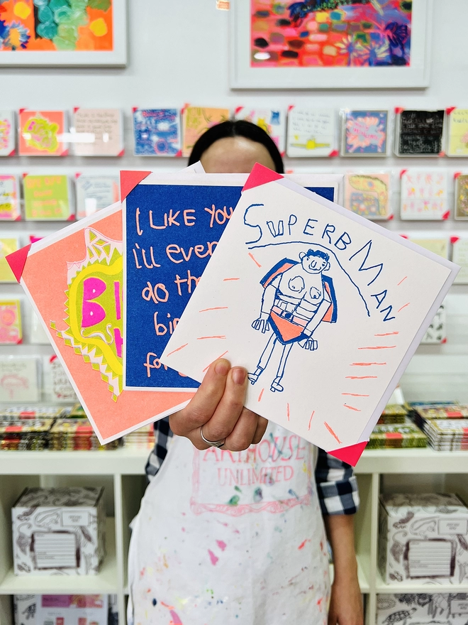 Artist holding the Superbman riso printed charity father's day card with a picture of a man in a cape