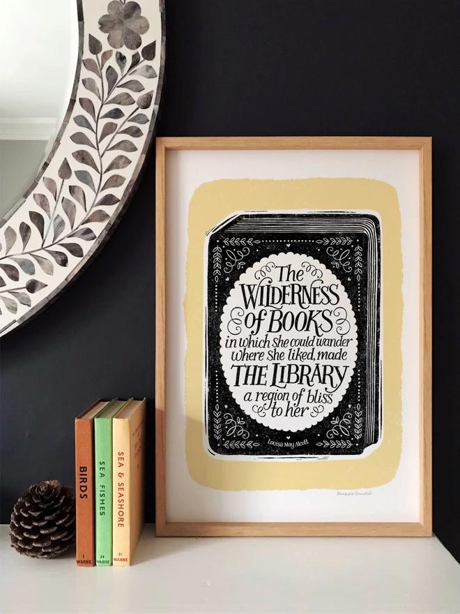 black and yellow book quote print in a wood frame against a dark wall