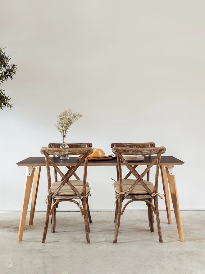 A stylish and minimalist dining table with Fenix top, coloured steel brackets and solid oak legs, with four antique chairs around it.