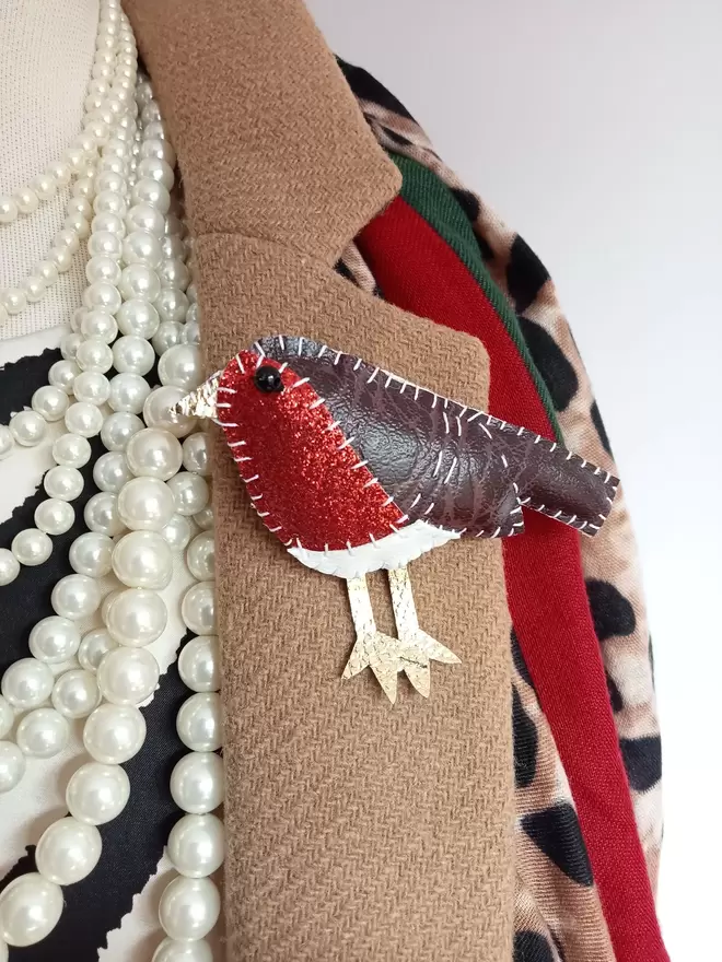 A leatherette hand stitched plump robin brooch, pinned onto a camel coat, worn with strings of pearls