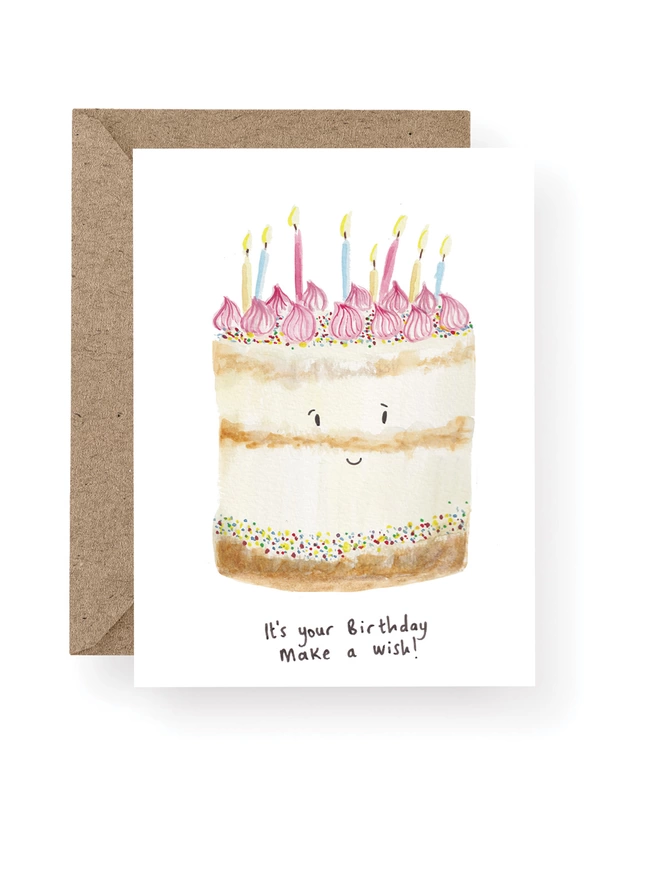 Birthday Cake Card, Card Has a White Base With Hand Painted Birthday Cake adorned with Candles and a Smiley Face.  Sitting On A Recycled Brown Kraft Envelope.  There Is Black Handwritten Text Underneath The Cake Which Reads ‘ It’s your birthday, make a wish!’