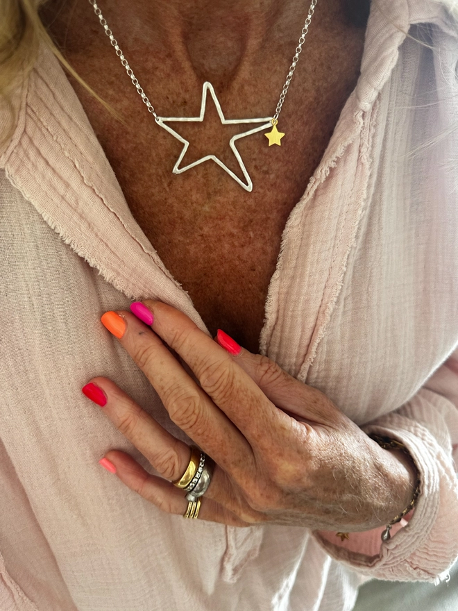 model wears a large silver open star charm on a silver chain with gold mini star charm