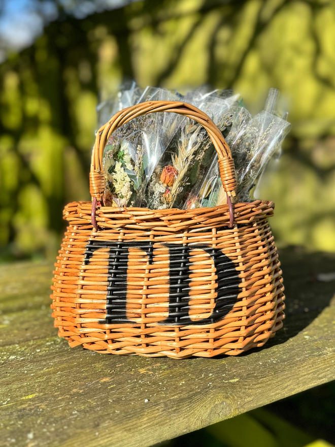 Personalised child's wicker basket "TD" displayed outside with flowers in