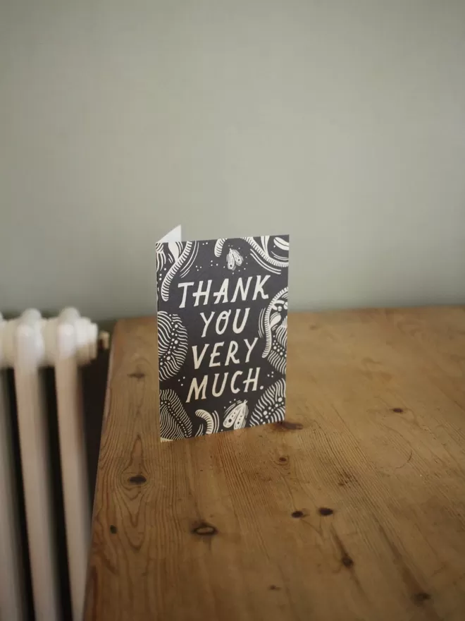 Black and white greeting card with illustration and the words thank you very much written on it stood up on a wooden table