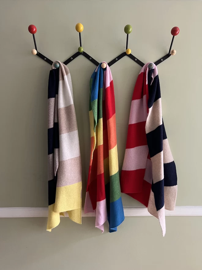 A collection of brightly coloured scarves hanging on coat hooks