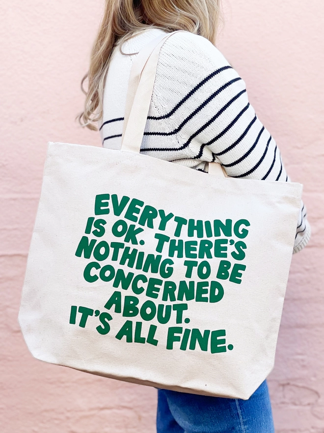 model holding a large natural canvas tote bag bearing the words Everything is OK. There's nothing to be concerned about. It's all fine.