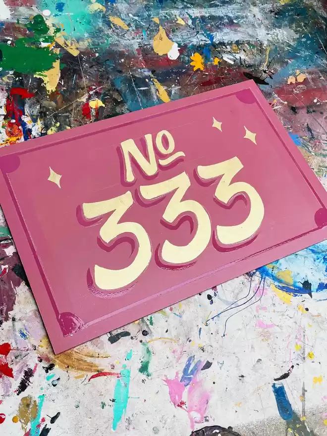 'No. 333' on a pink background with golden letters and stars with dark pink drop shades and details.
