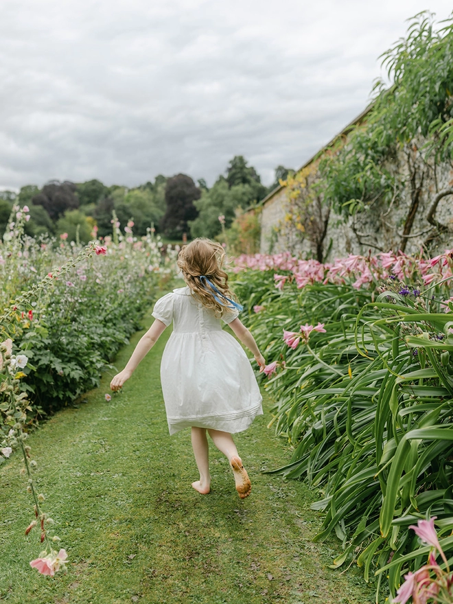A little girl runs through a garden with a white dress on