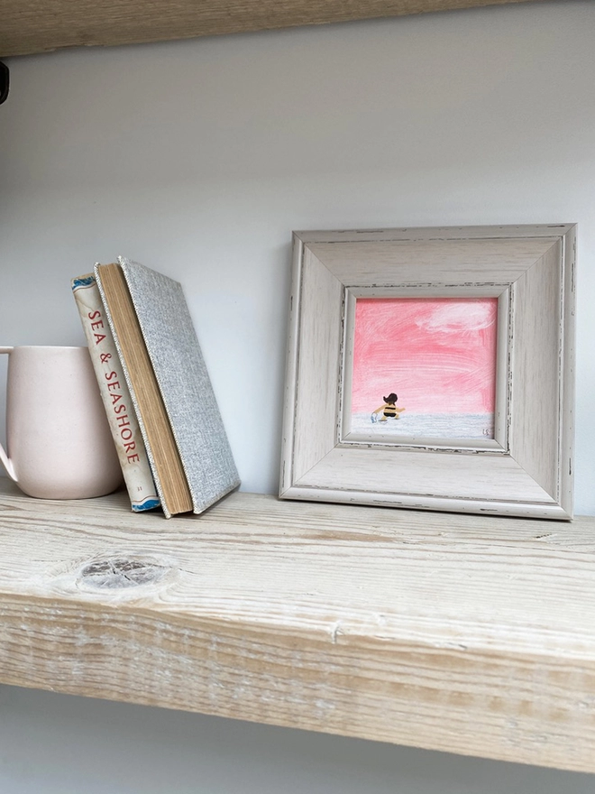 pale wooden shelf with painting of sunset and swimmer in chunky pale grey frame