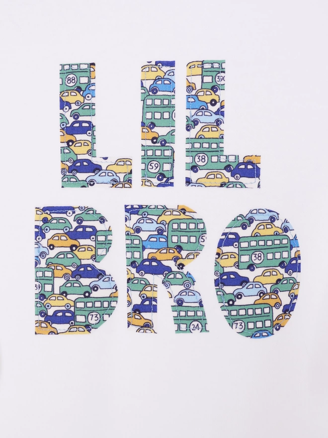Lil Bro appliquéd on a white cotton baby romper in a vintage cars and busses Liberty print. A close up of the stitching