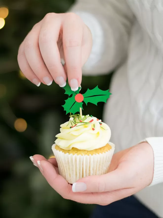 Model places paper holly decoration into cupcake