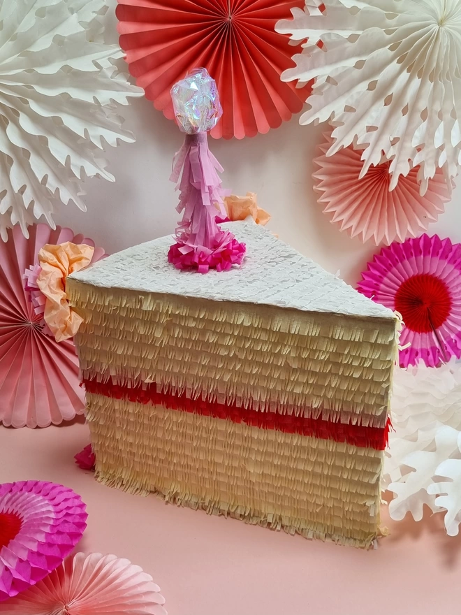 slice of cake pinata with pink candle on a background of pink paper fans