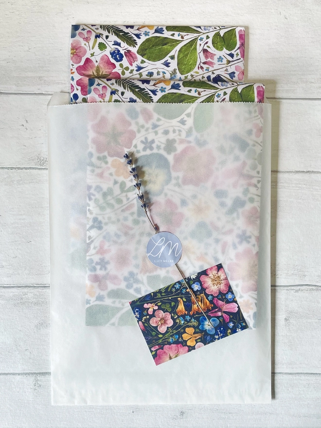 Glassine envelope with two folded sheets of recycled floral gift wrap paper, Lucy Miller branded sticker, and lavender sprig