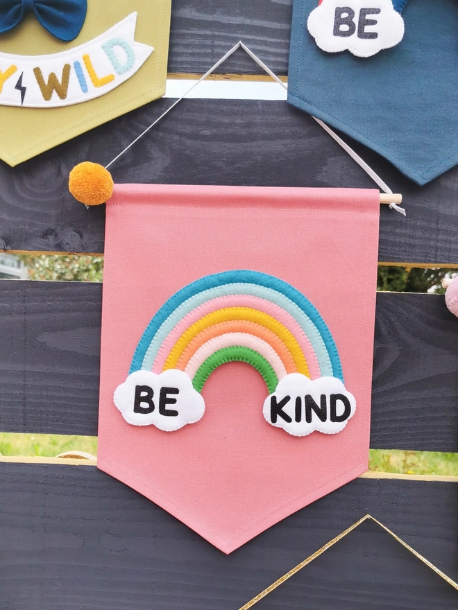 Pink be kind banner hanging from a garden fence