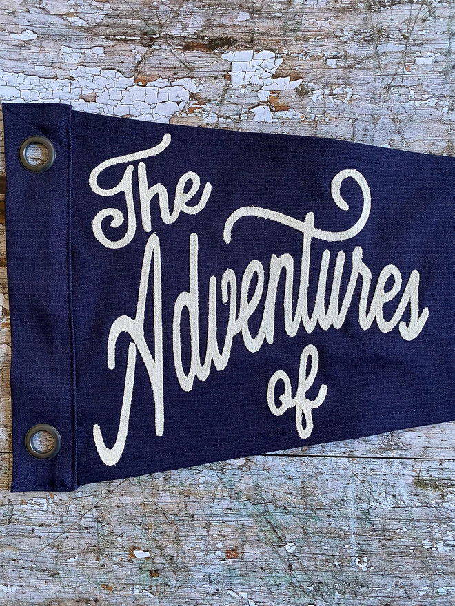 A close up detail of a 'The adventures of' navy pennant with ivory lettering