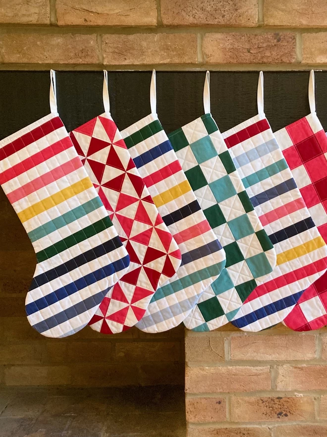 A range of Cooper and Fred Quilted Stockings seen hanging on a fireplace.