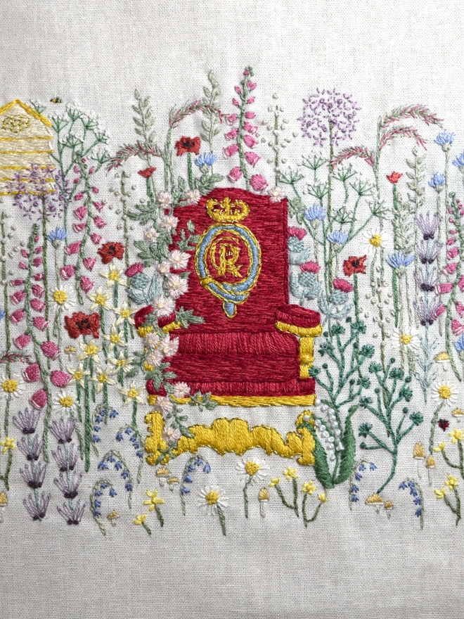 King Charles' Crimson State Throne sits amongst British Wildlife of Honey Bees, Ladybird, Hedgehog in a British Meadow of Foxgloves, Poppies, Lavender, Allium, a Beehive in the background and British National flowers grow around the throne.
