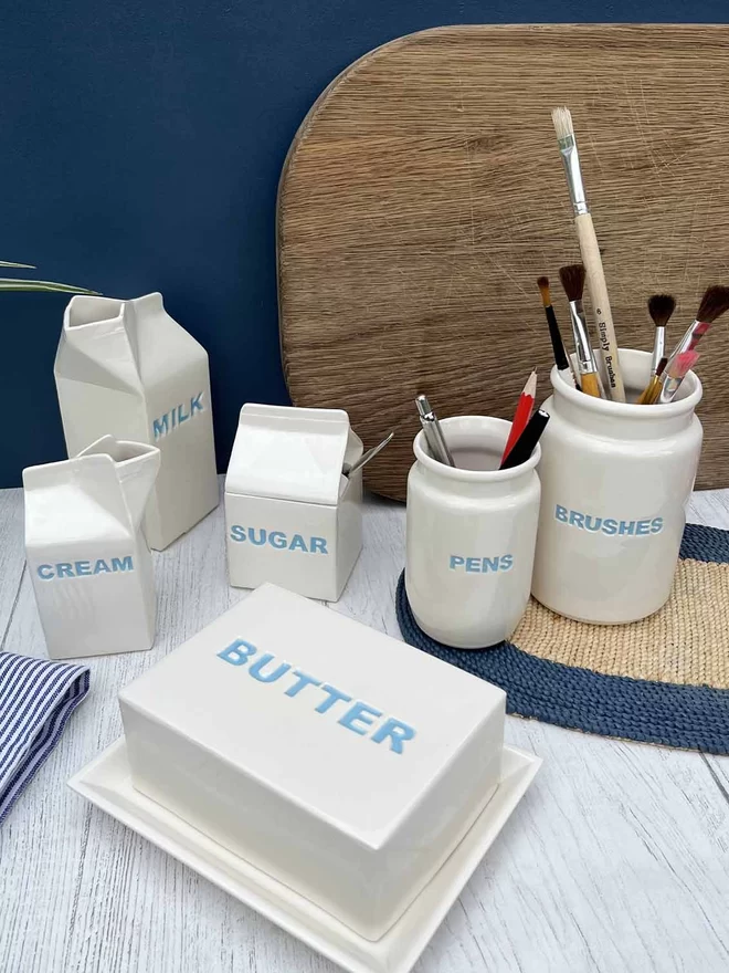 A handmade brushes jar stands with matching pens pot, butter dish, milk and cream cartons.