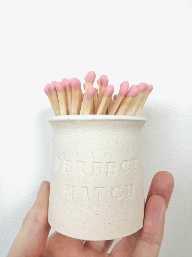hand holding match pot with perfect match stamped on the front. match pot contains peach coloured matches