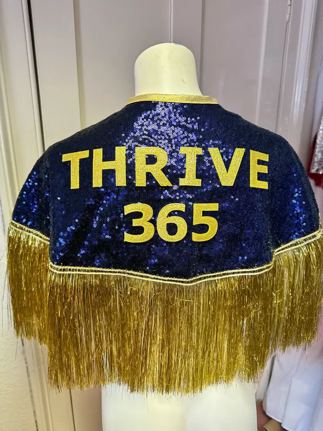 a midi cape with navy sequins, gold text reading 'THRIVE 365' and gold tinsel