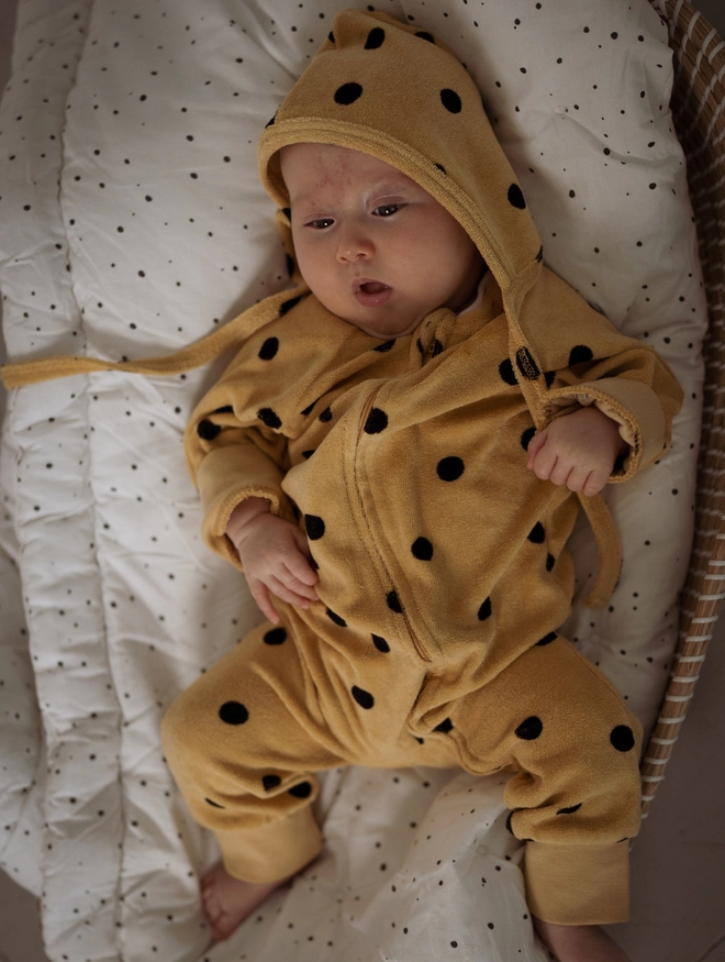 Baby wearing the Another Fox Camel Terry Towel Spot Baby Sleepsuit lying in a cot. 