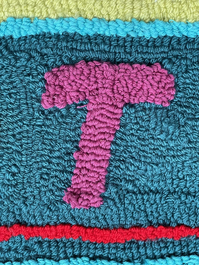 Purple wool loops making a "T" on a blue loop background with pink stripe underneath