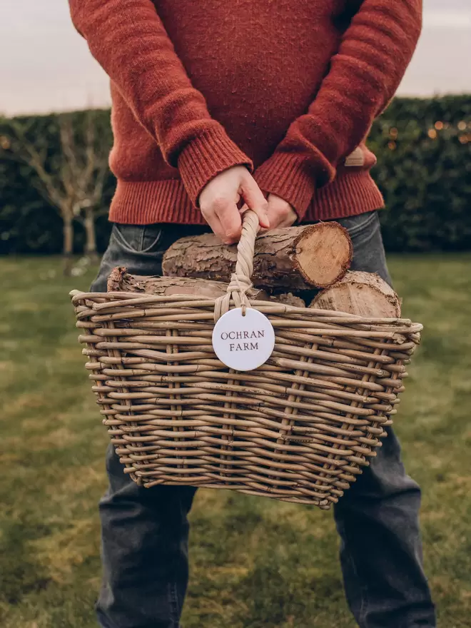 Person holding a wicker log basket with ceramic tag