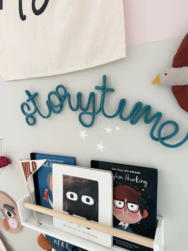 "storytime" wall hanging for kids who love to read books hanging up over a book shelf. 