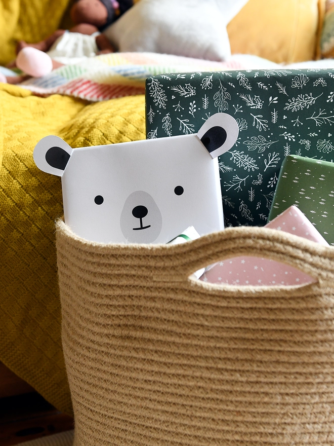 A gift wrapped in polar bear wrapping paper is tucked into a woven basket along with several other wrapped gifts.