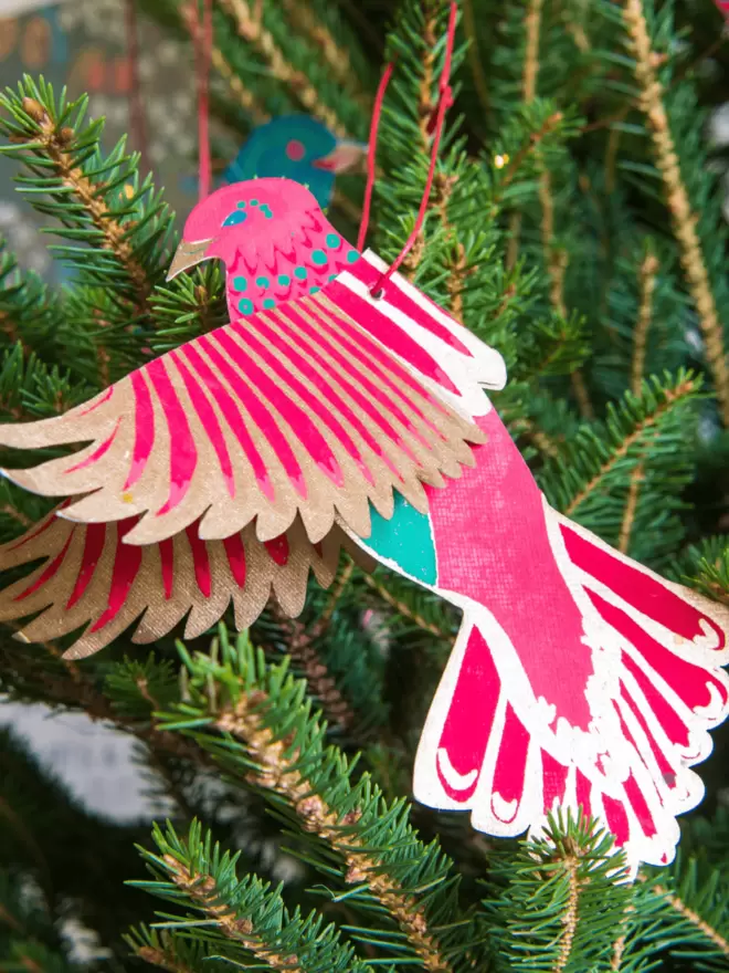 Gold, pink and teal paper bird hanging on Christmas tree